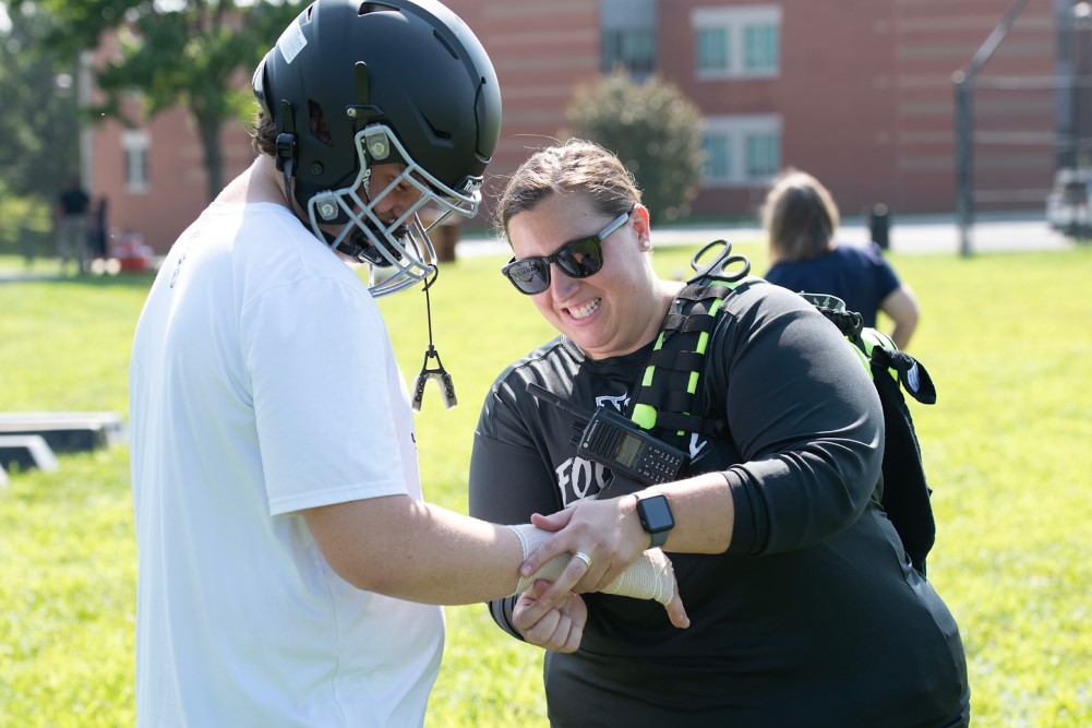 Entrenador atleta ayudando a un estudiante atleta en el campo. Crédito: MCPS.