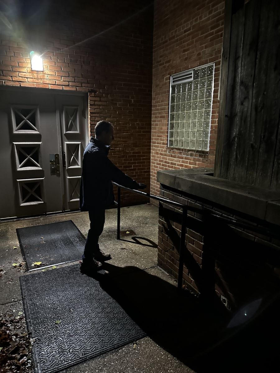 夜间时间点步行时，议会主席格拉斯站在一座漆黑的建筑物外面