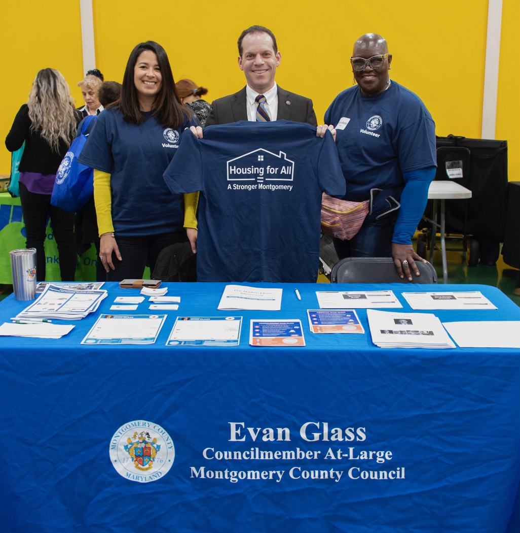 El presidente del Concejo Glass, posa con voluntarios sosteniendo una camiseta que dice Vivienda para todos.