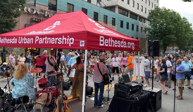 Músicos tocando bajo la carpa de la organización conocida como Bethesda Urban Partnership en un concierto concurrido al aire libre.