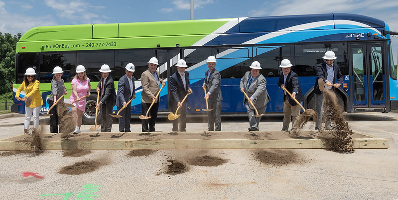 Des élus et des responsables du secteur des transports pellettent de la terre pour la cérémonie d'inauguration du dépôt de bus, devant un bus Ride On.