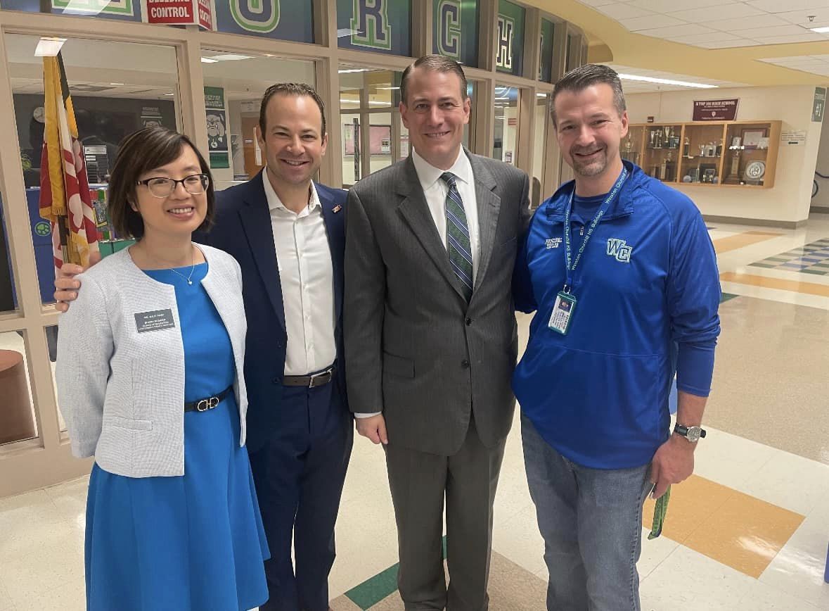 De gauche à droite : Mme Yang, M. Friedson, le surintendant Taylor et le directeur de l'école Churchill, M. Taylor, sourient à l'intérieur du bâtiment scolaire.