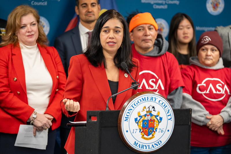 Council President Fani-González speaks at a podium with CASA members and county leaders standing behind her.
