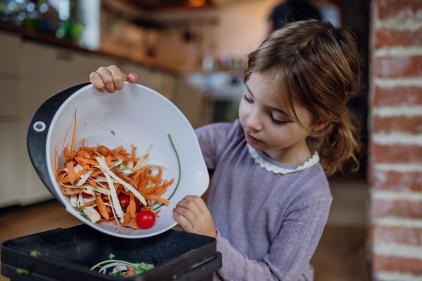 young child placing food scraps in kitchen composting bin