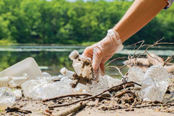 gloved hand picking up plastic water bottle litter from waterway