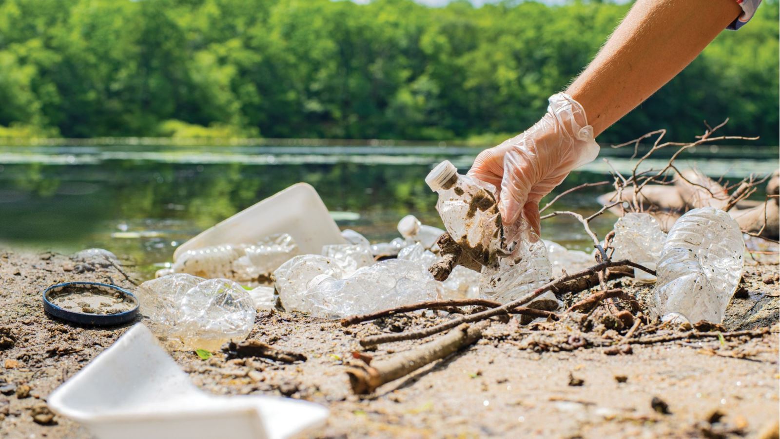 gloved hand picking up plastic water bottle in waterway