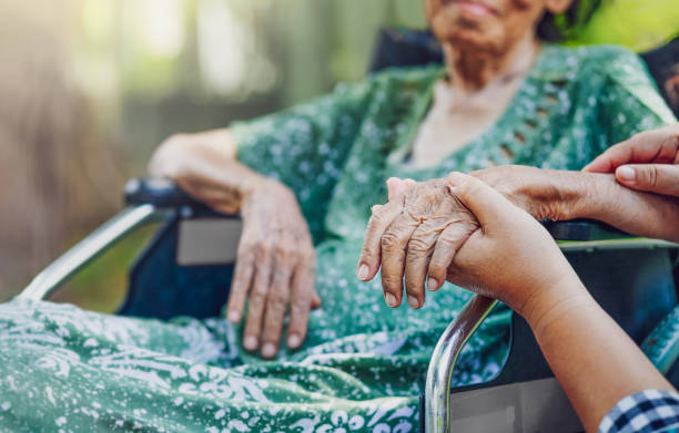 Elderly women in a wheelchair holding hands with a nurse