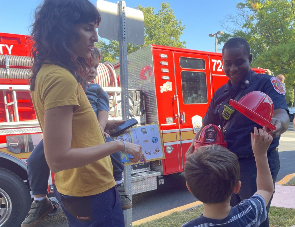 woman and two children speaking to a firefighter in front of a firetruck