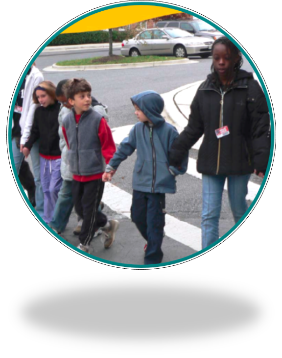 A teen student helps elementary school students cross the road in a crosswalk