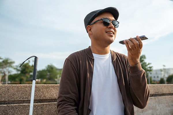 Young blind man using application on mobile phone sharing information on accessibility for persons with visual impairment. He is using a white cane. 