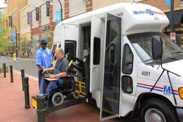 an adult male who is using a wheelchair is exiting MetroAccess van on a vehicle lift