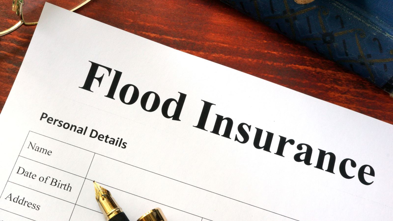 Paper flood insurance application on a desk with eyeglasses and fountain pen.