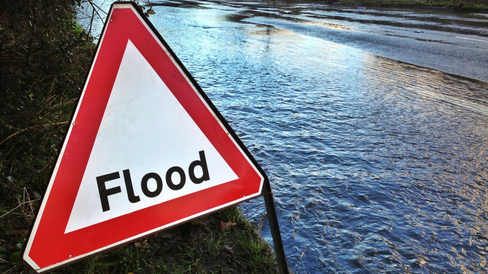 White and red triangle flood road sign in front of flooded road