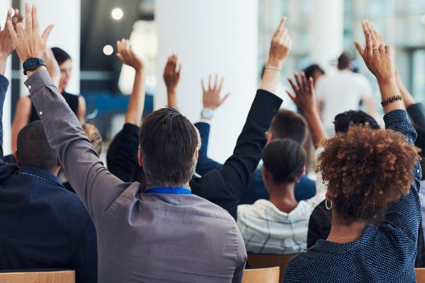 Room filled with people in professional clothing raising hands to ask questions.