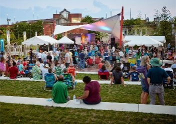 A photo several people sitting and standing in groups with tents at an outdoor event