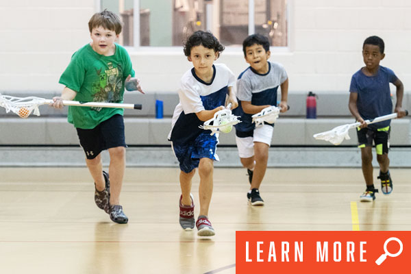 Young boys learning lacrosse indoors. View lacrosse information.