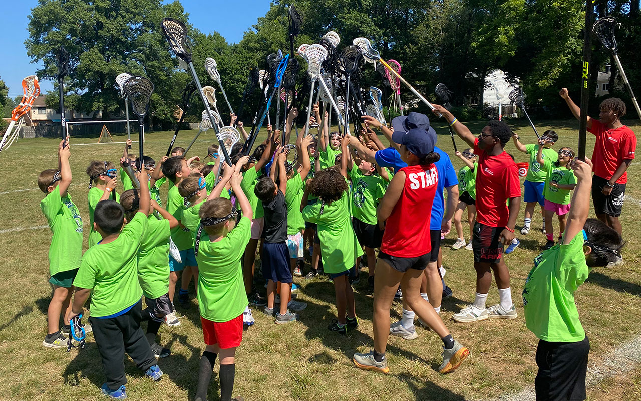 group of kids raising their lacrosse sticks together